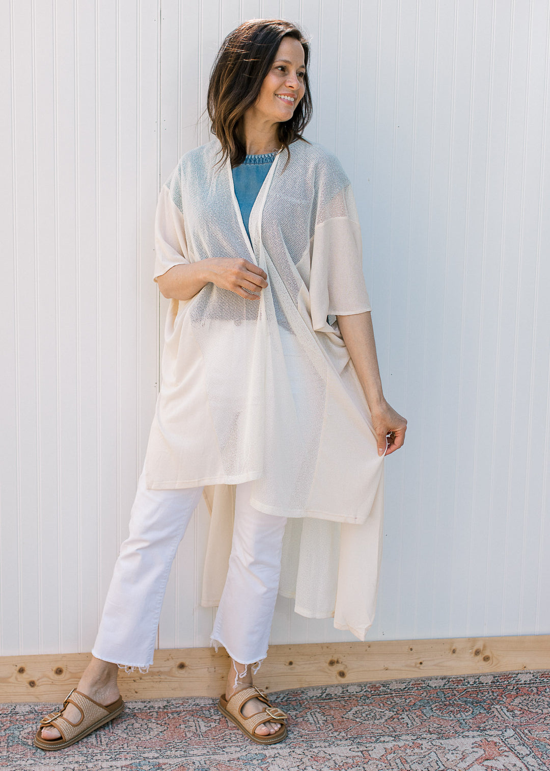 Model wearing a blue top with a cream, maxi length duster with a sheer woven fabric.