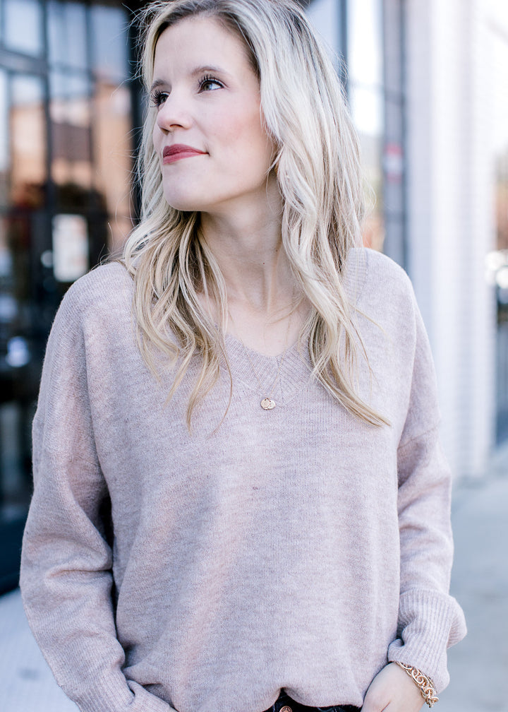 Close up of v-neck on a wheat colored sweater with extended shoulder and long sleeves.