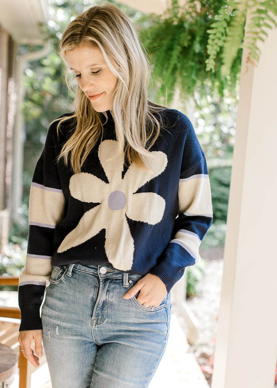 Model wearing a navy sweater with a cream daisy and cream stripes on long sleeves.