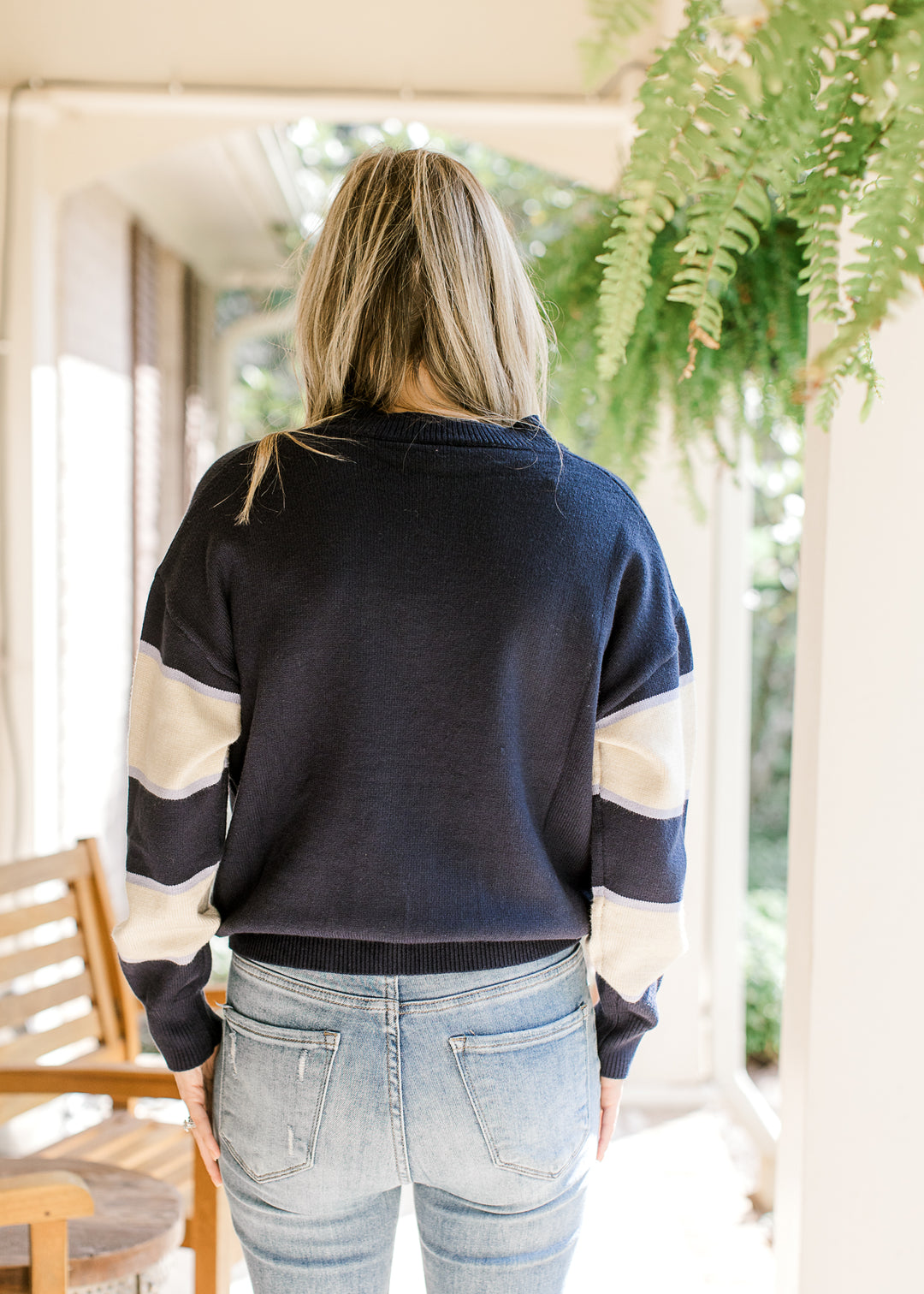 Back view of Model wearing a navy sweater with a cream daisy and cream stripes on long sleeves.