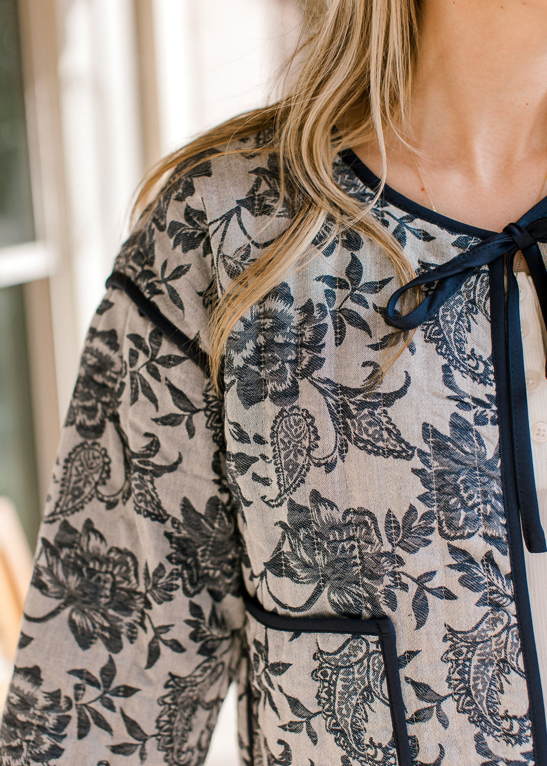 Close up of tie closure and quilted fabric on a gray jacket with navy floral and long sleeves.