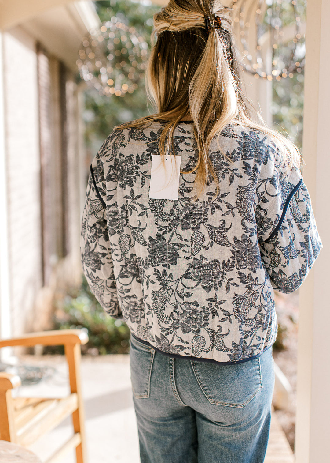 Back view of model wearing a gray jacket with navy floral pattern, long sleeves and a tie closure.