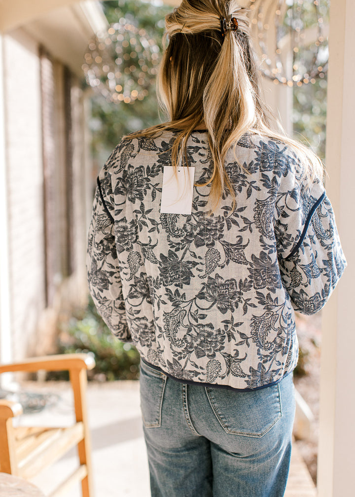 Back view of model wearing a gray jacket with navy floral pattern, long sleeves and a tie closure.