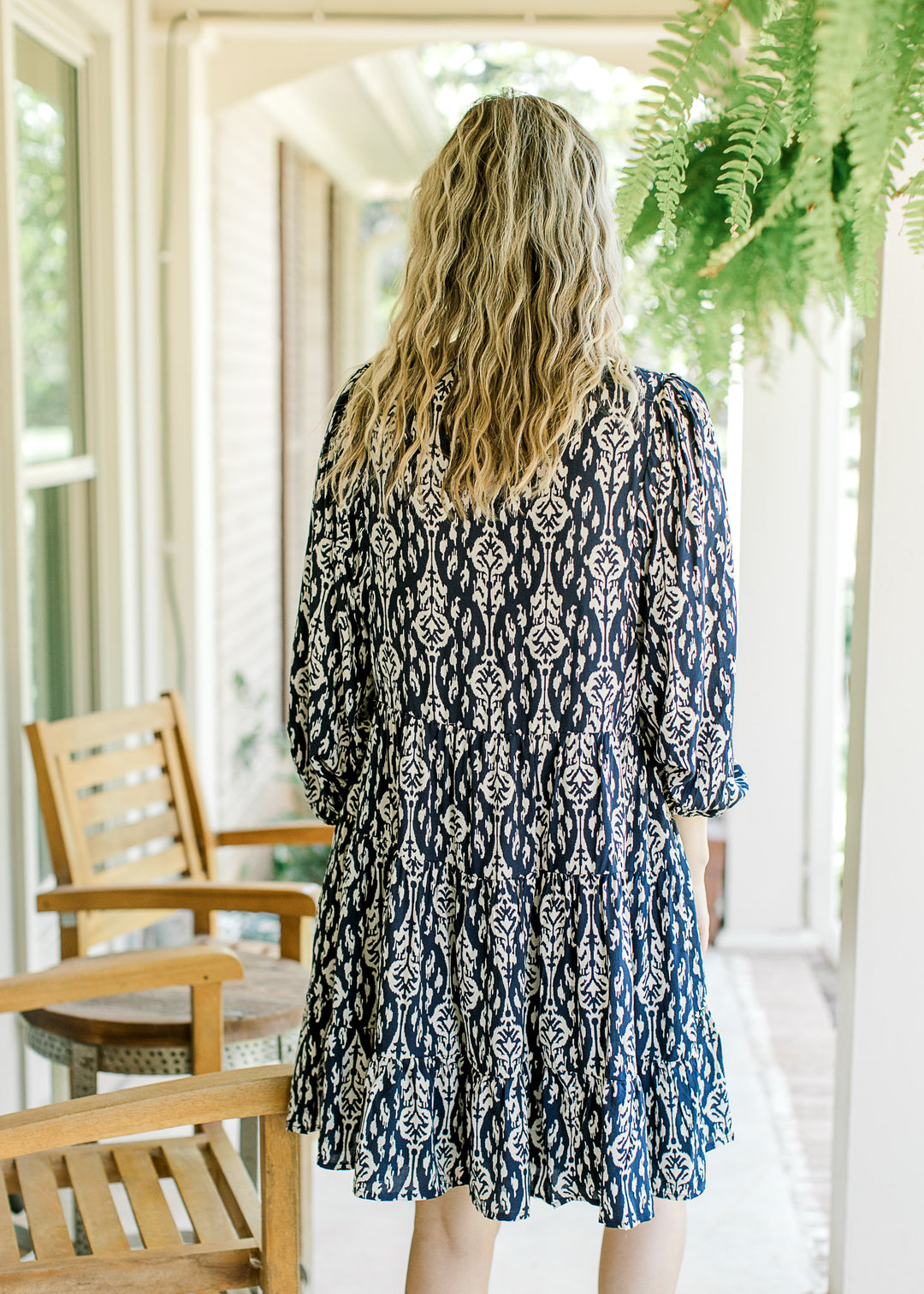 Back view of Model wearing a navy dress with taupe floral pattern, 3/4 sleeve and a v-neck.