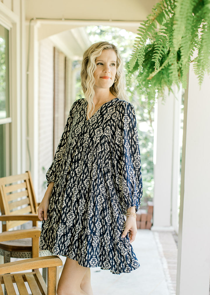 Model wearing a navy above the knee dress with taupe floral pattern and 3/4 sleeve.