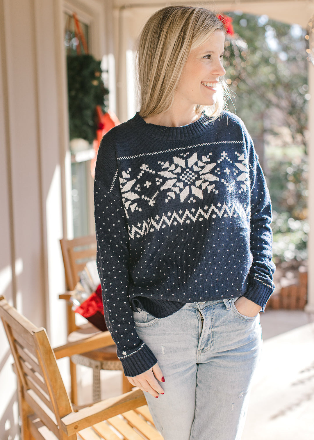 Model wearing jeans and a navy sweater with a  snowflake pattern, long sleeves and a vintage feel.