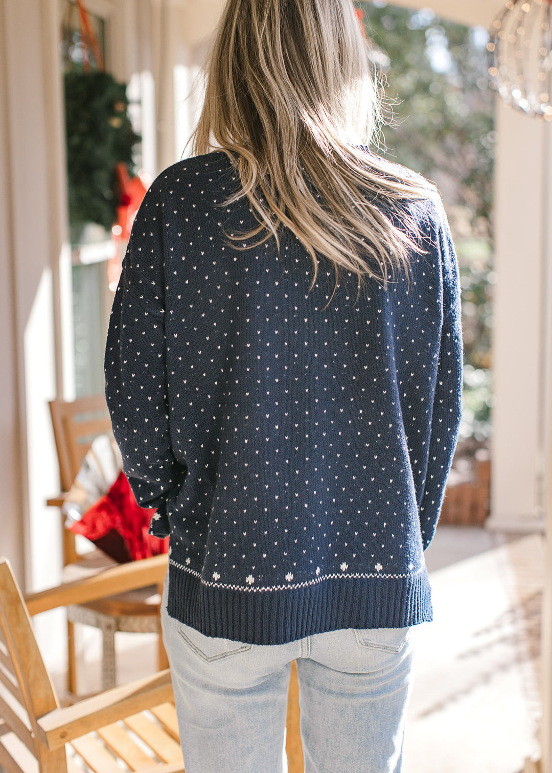 Back view of Model wearing a navy sweater with a  snowflake pattern and long sleeves.