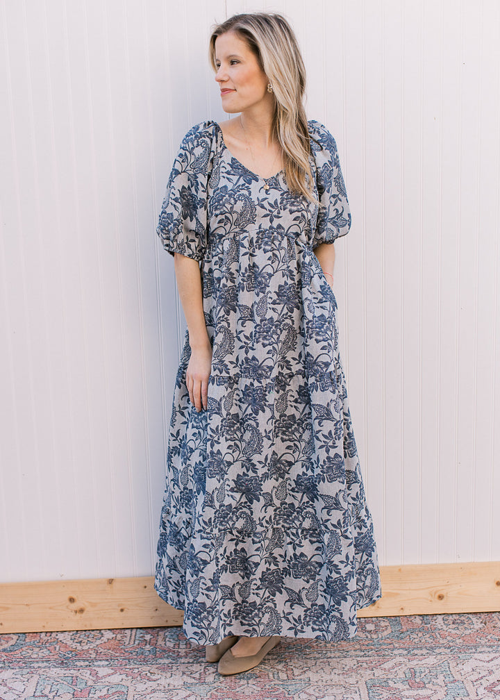 Model wearing a gray, v-neck maxi with navy floral, short puff sleeves and an elastic waist.