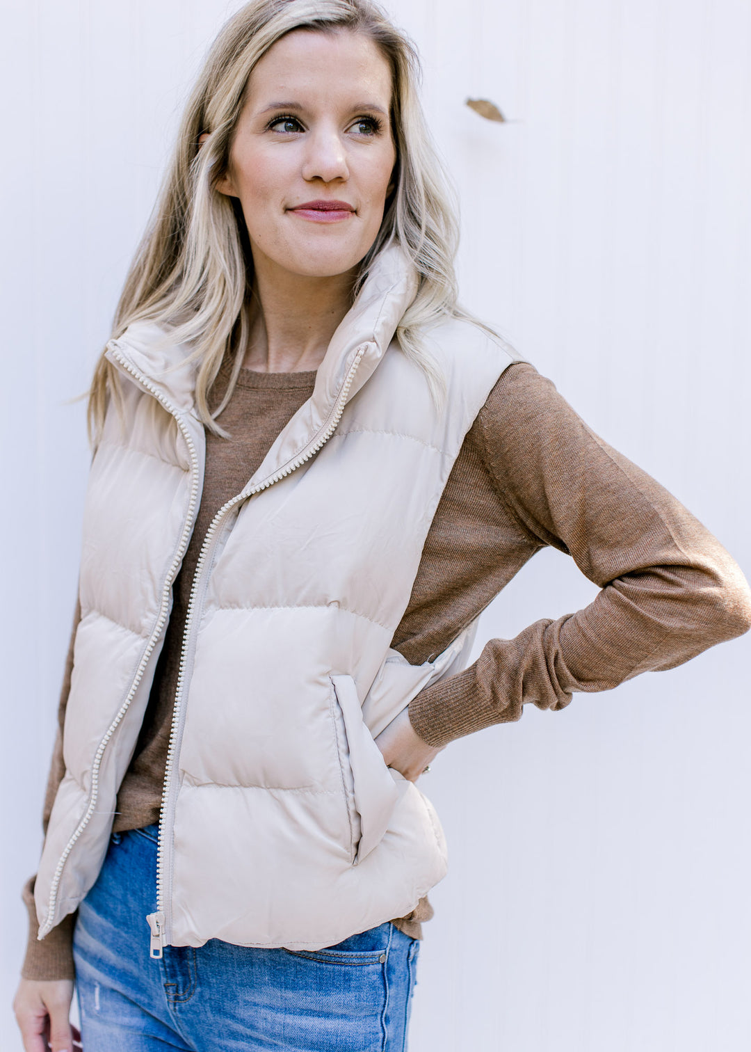 Model wearing an oatmeal puffer vest with a zip front, slightly cropped fit and cuff pockets.