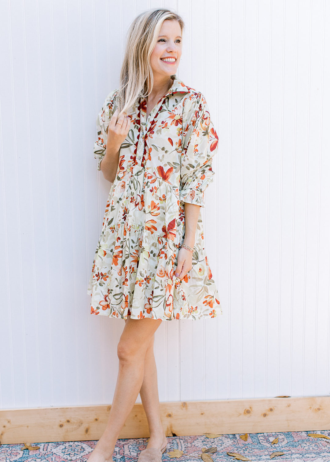 Model wearing a cream dress with olive and rust floral, 3/4 poet sleeve and a collar.