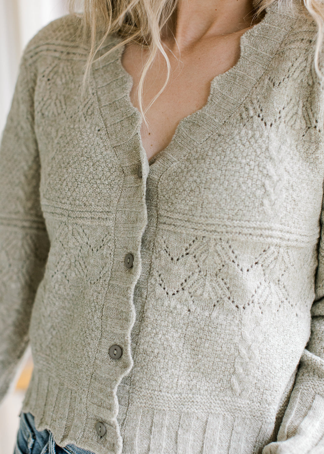 Close up of scalloped edging and buttons on a soft olive cardigan with long sleeves.