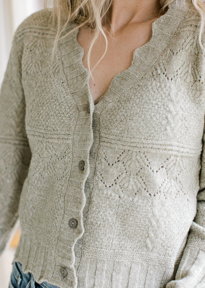 Close up of scalloped edging and buttons on a soft olive cardigan with long sleeves.