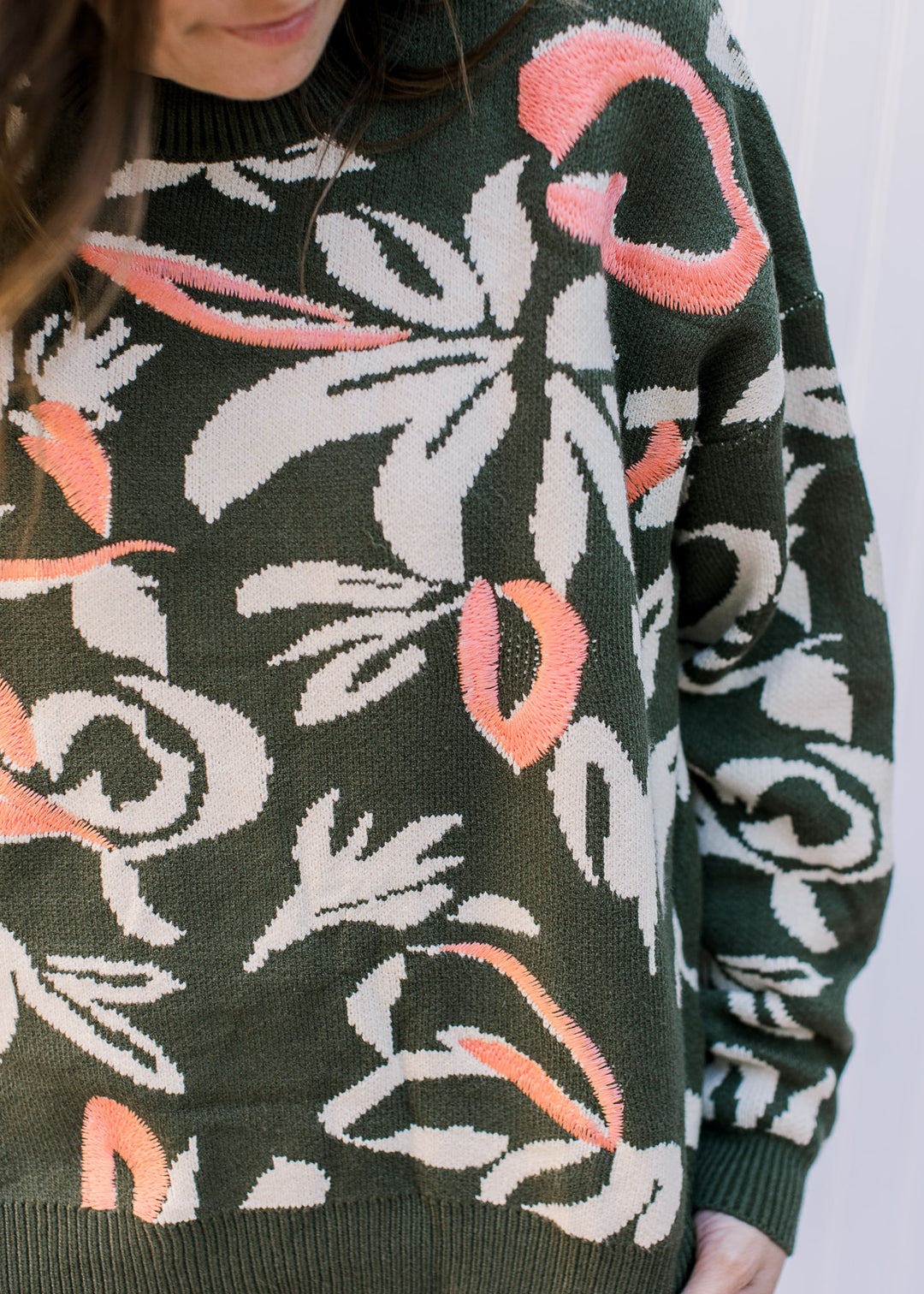 Close up of cream flowers and coral accents on an olive sweater with long sleeves.