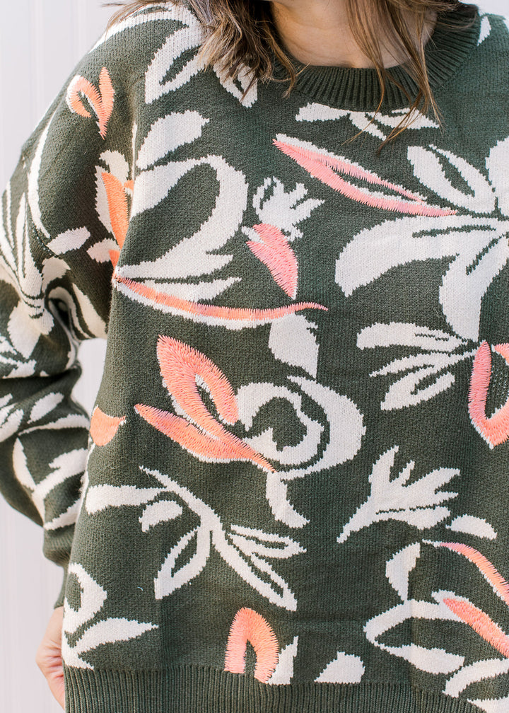 Model wearing a crew neck olive sweater with long sleeves and cream and coral floral.