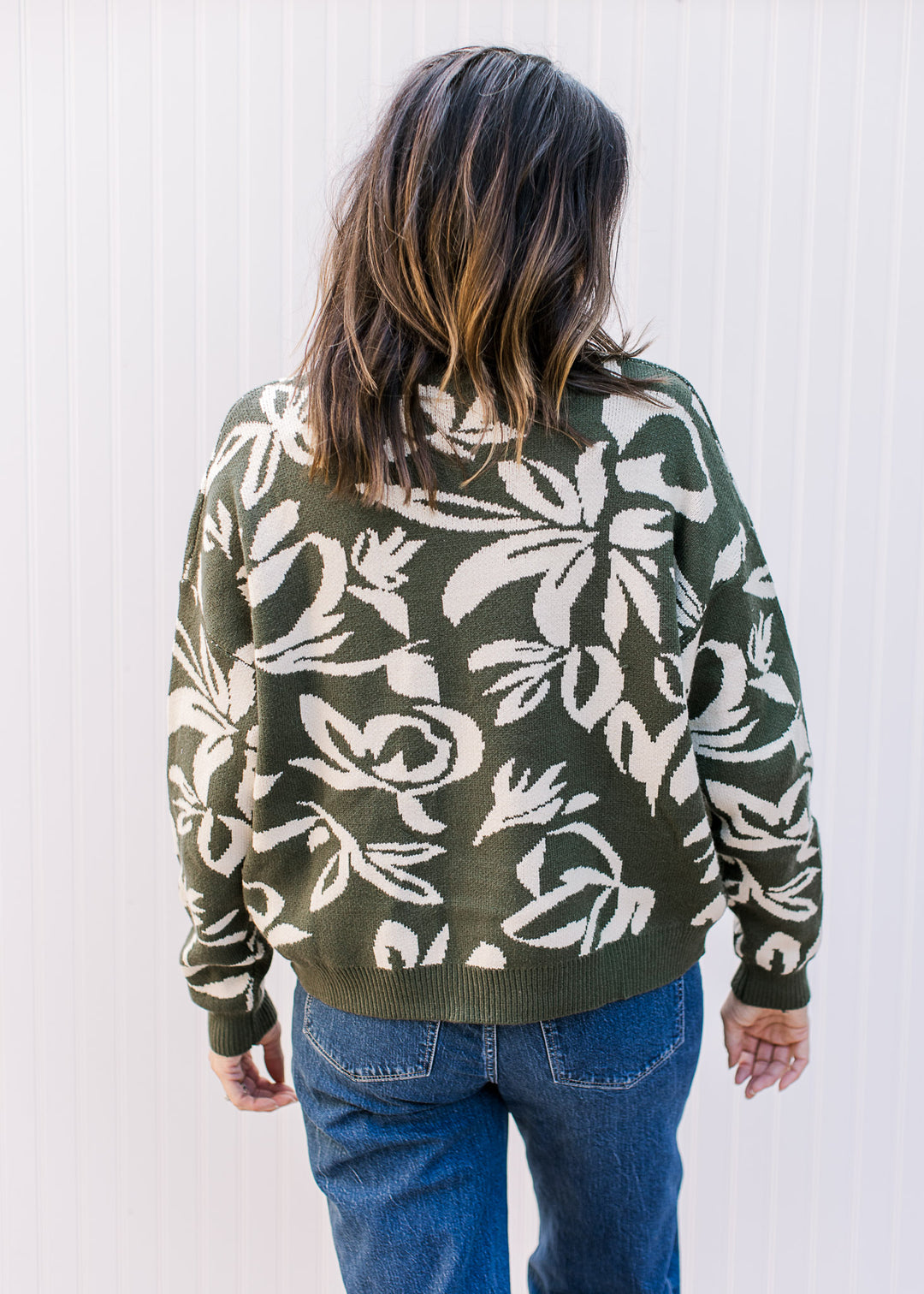 Back view of model wearing an olive sweater with cream floral and long sleeves.