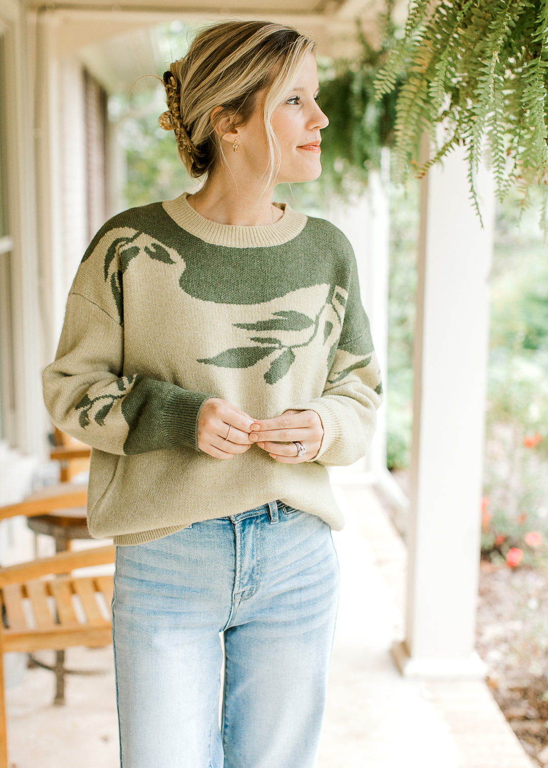 Model wearing a sage sweater with olive tree detail, long sleeves and round neck.