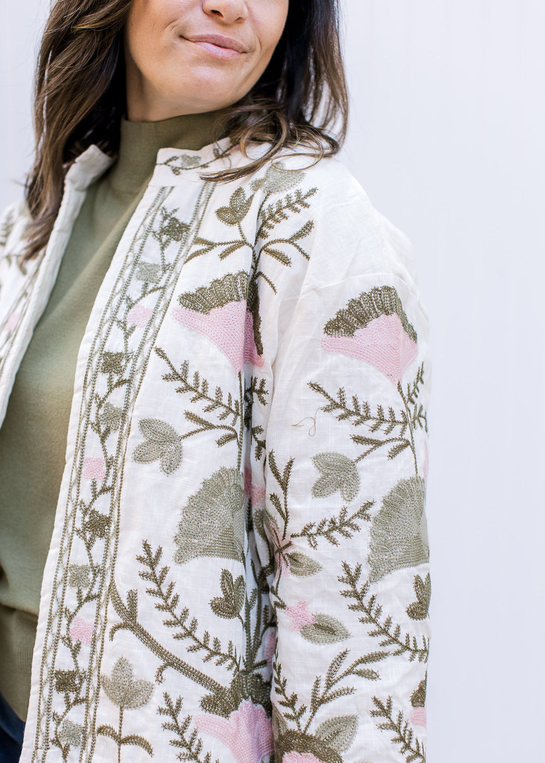 Close up of pink and green embroidered flowers on a cream long sleeve jacket with an open front.