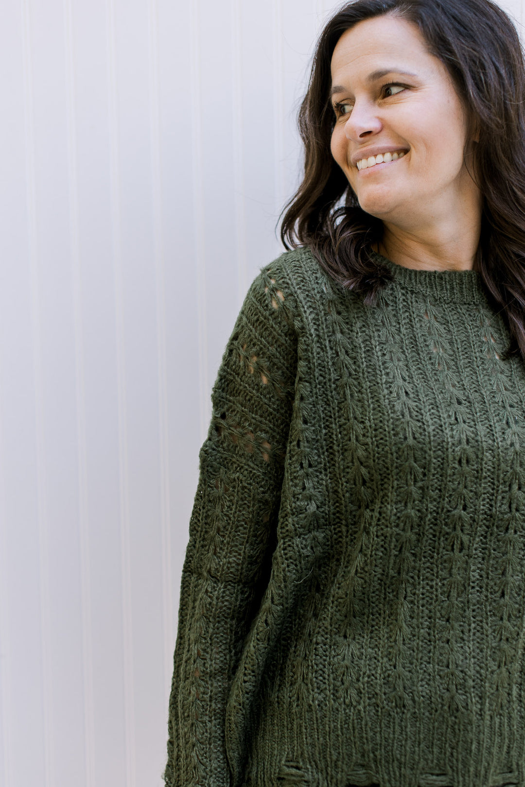 Close up of cable knit material on an olive sweater with distressed hem and cuff.