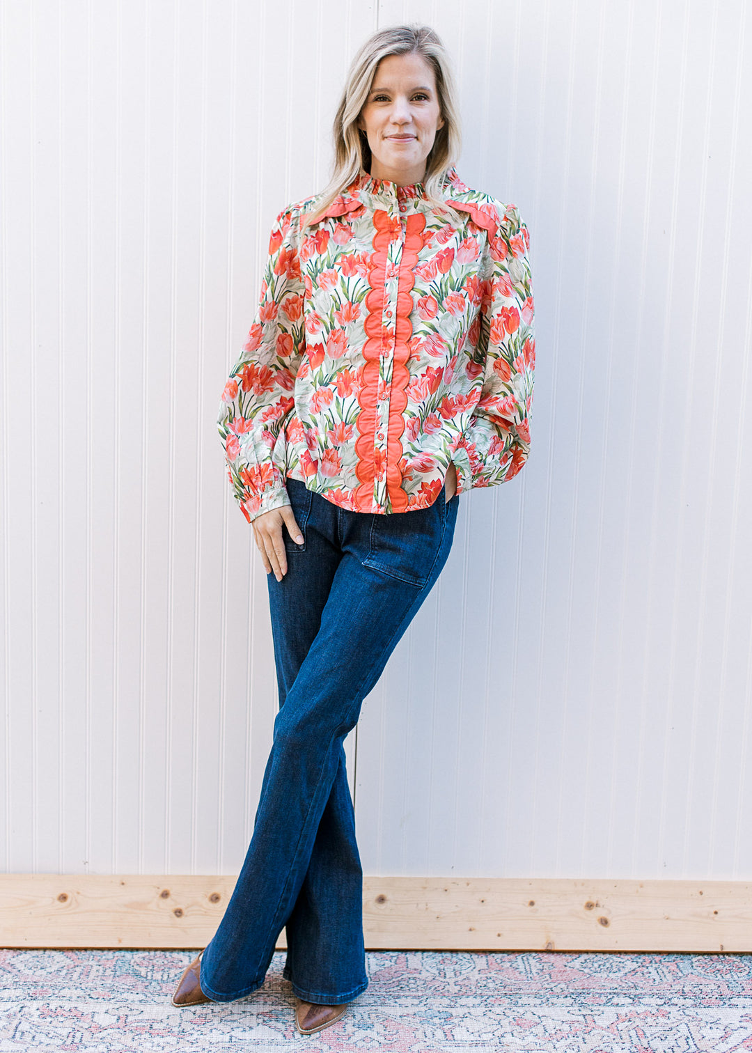 Model wearing jeans and a cream long sleeve top with pink tulips, coral scalloping and ruffle neck.