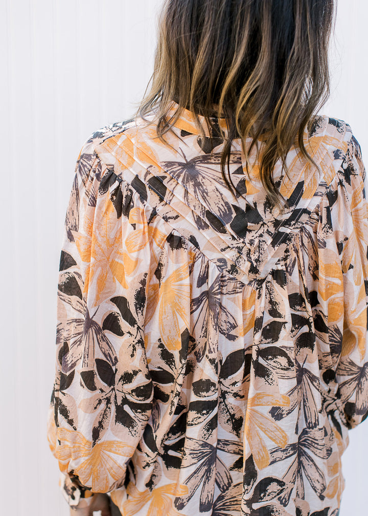 Back view of pleating along yolk on a cream long sleeve top with orange and brown flowers.