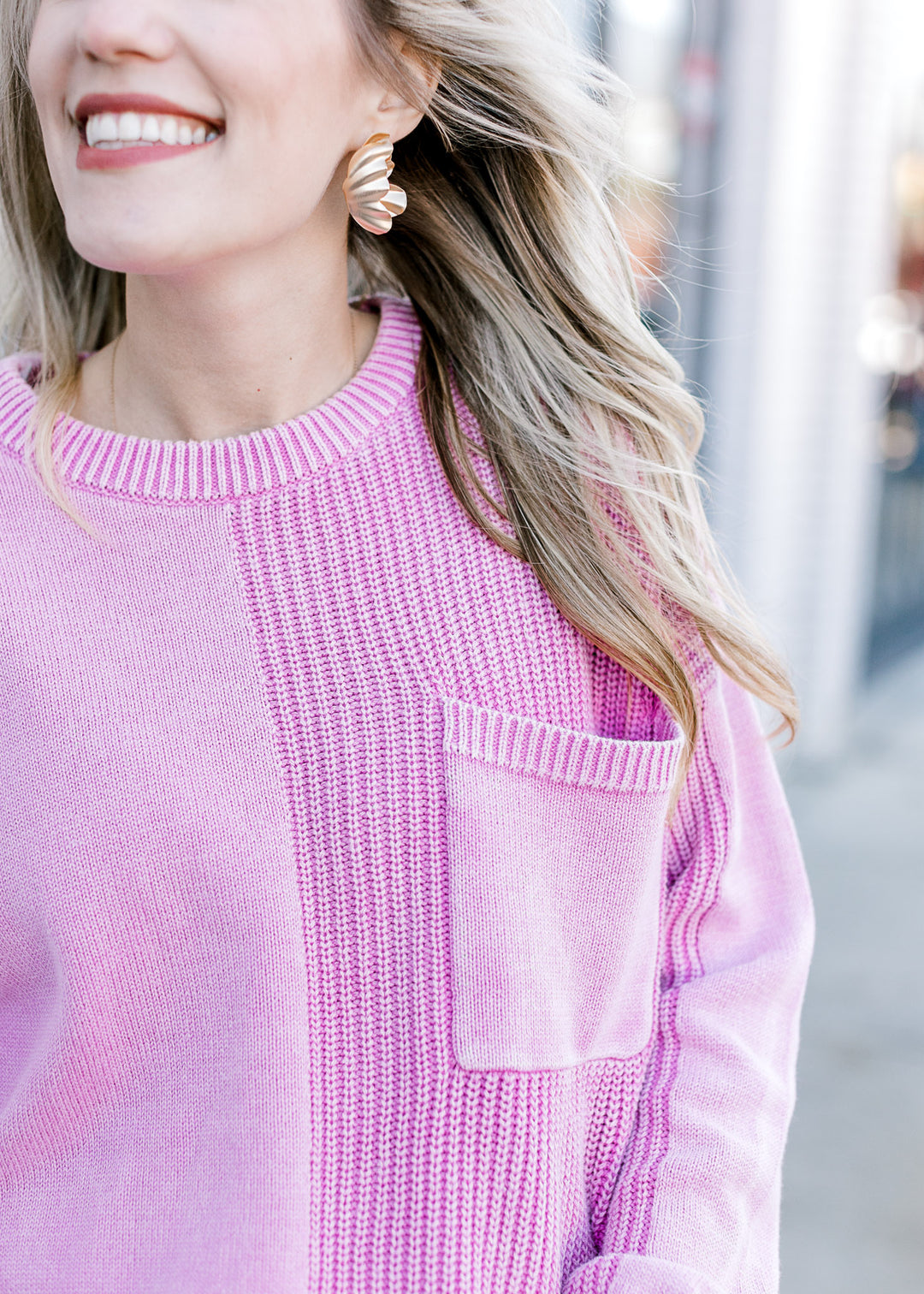 Close up of two styles of textured knit and a front patch pocket on a pink long sleeve sweater.