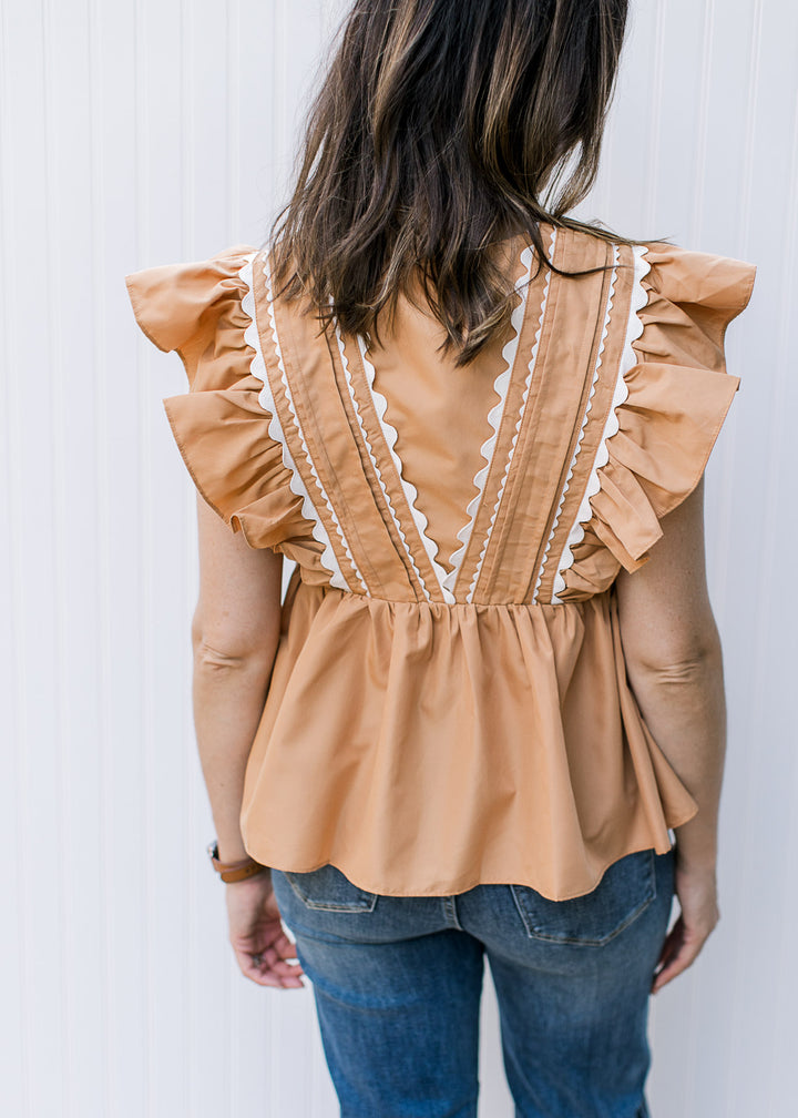 Back view of Model wearing a dusty orange top with ruffle cap sleeve and scallop white detail.