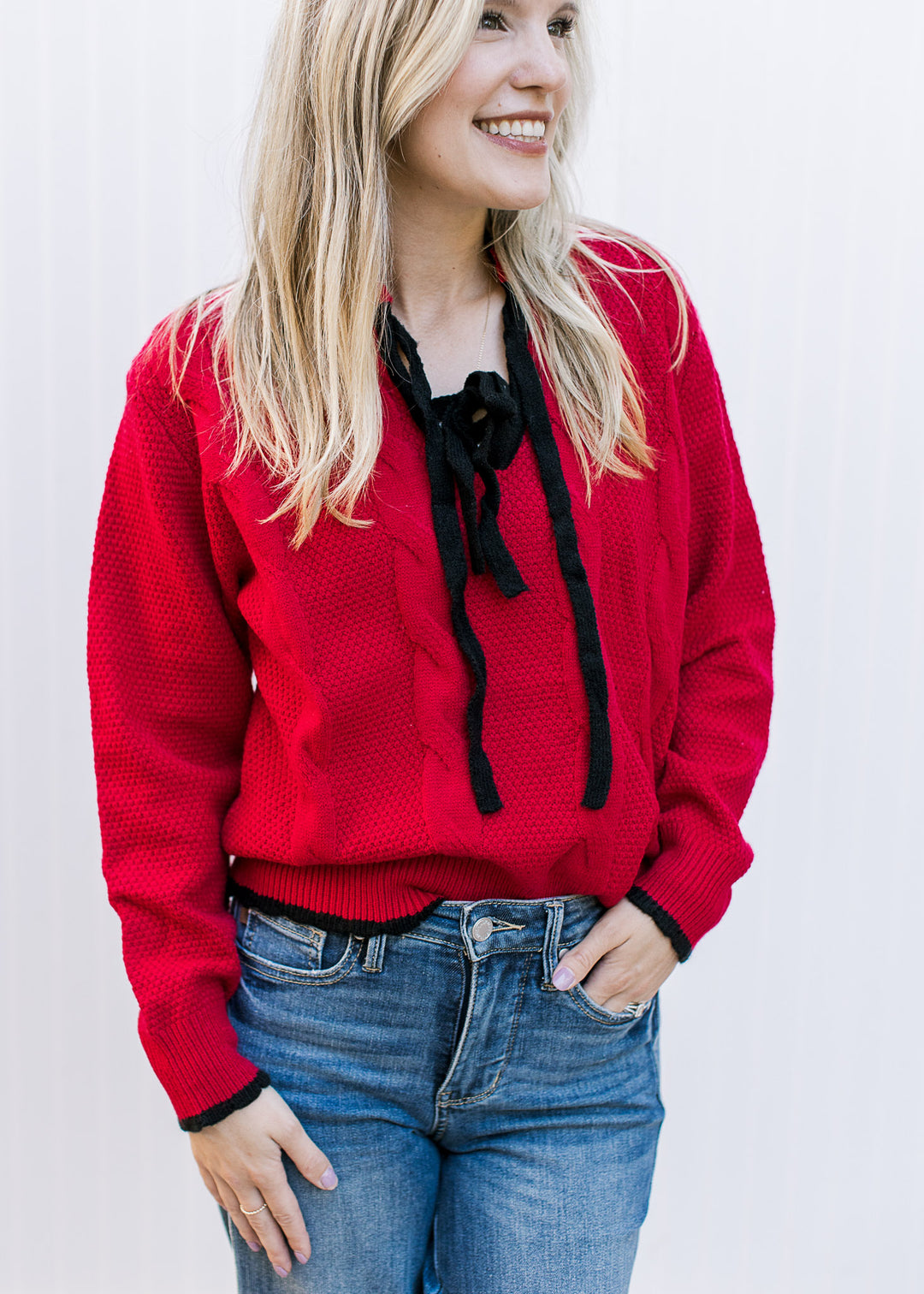 Model wearing a red knit sweater with black tie bow at v-neck and long sleeves.