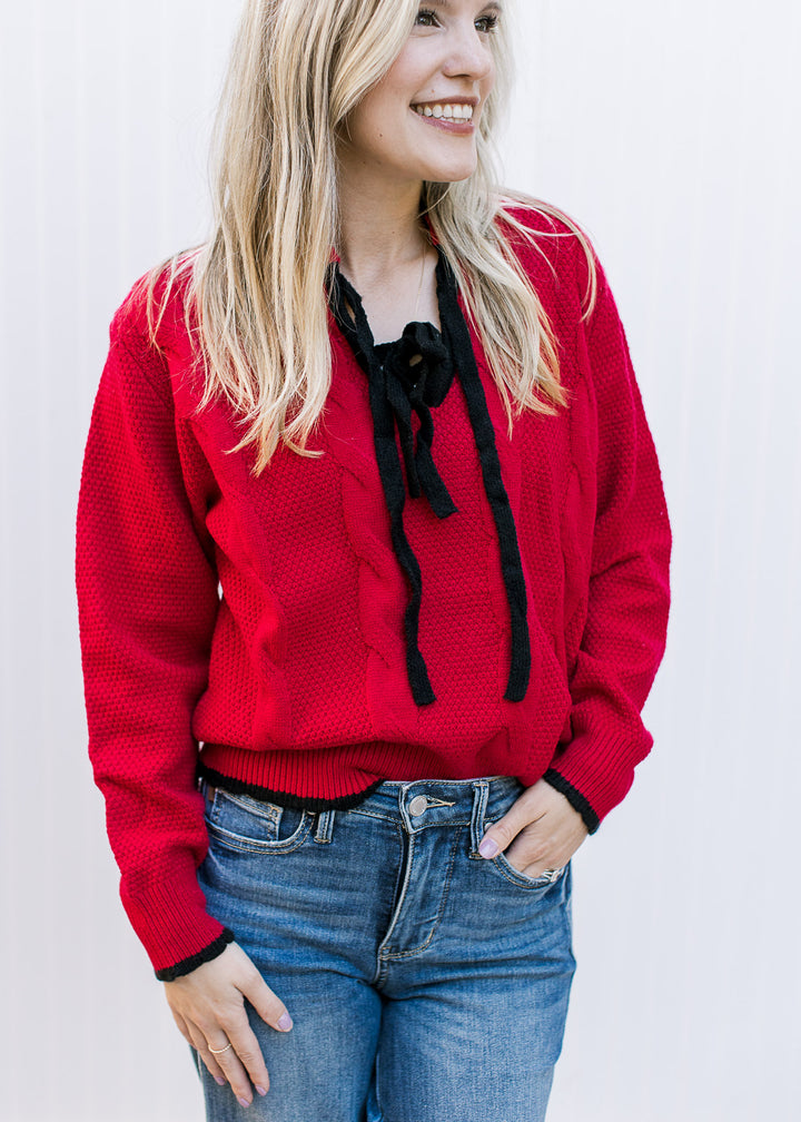 Model wearing a red knit sweater with black tie bow at v-neck and long sleeves.