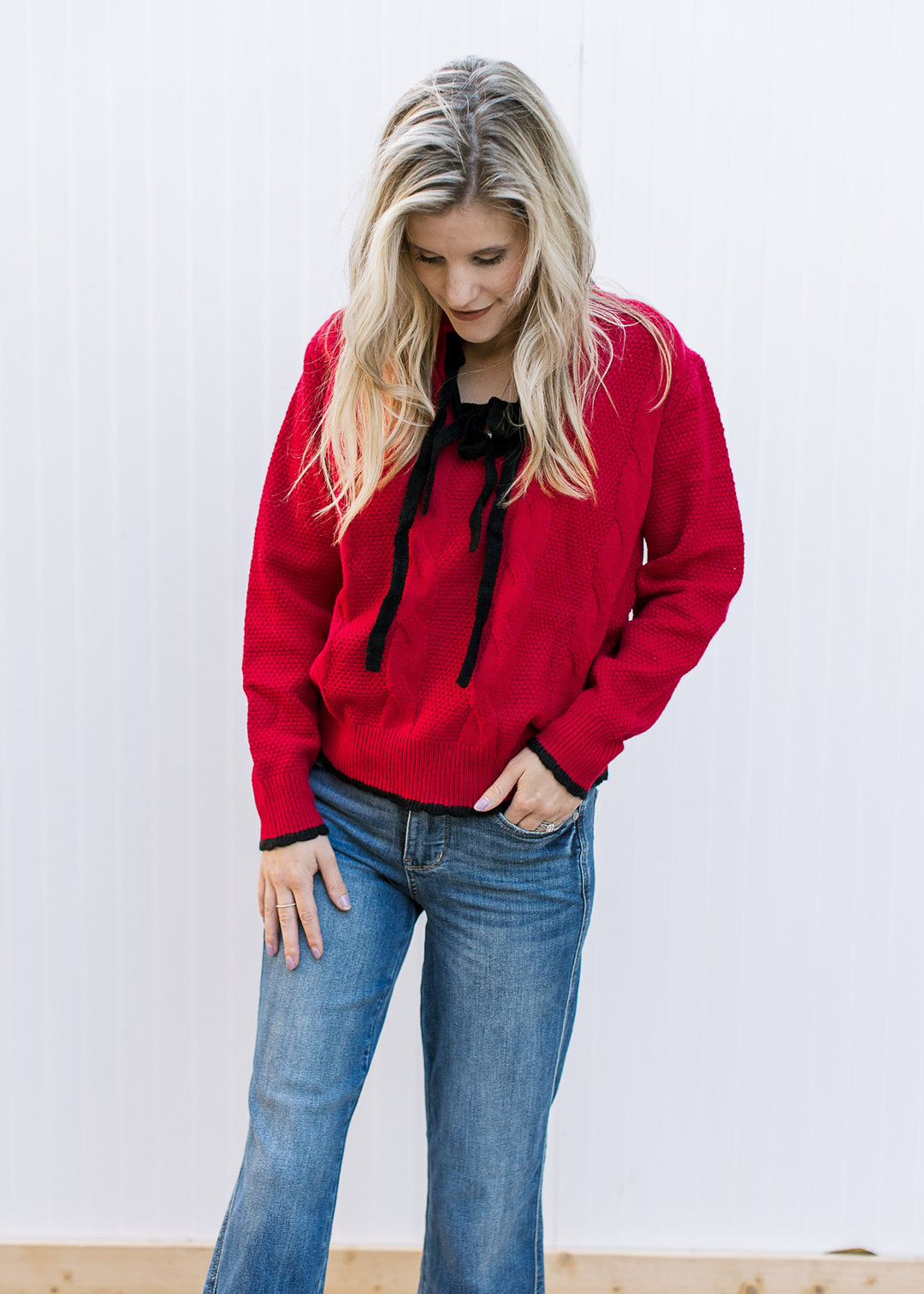 Model wearing jeans and a red knit sweater with black tie bow at v-neck and long sleeves.