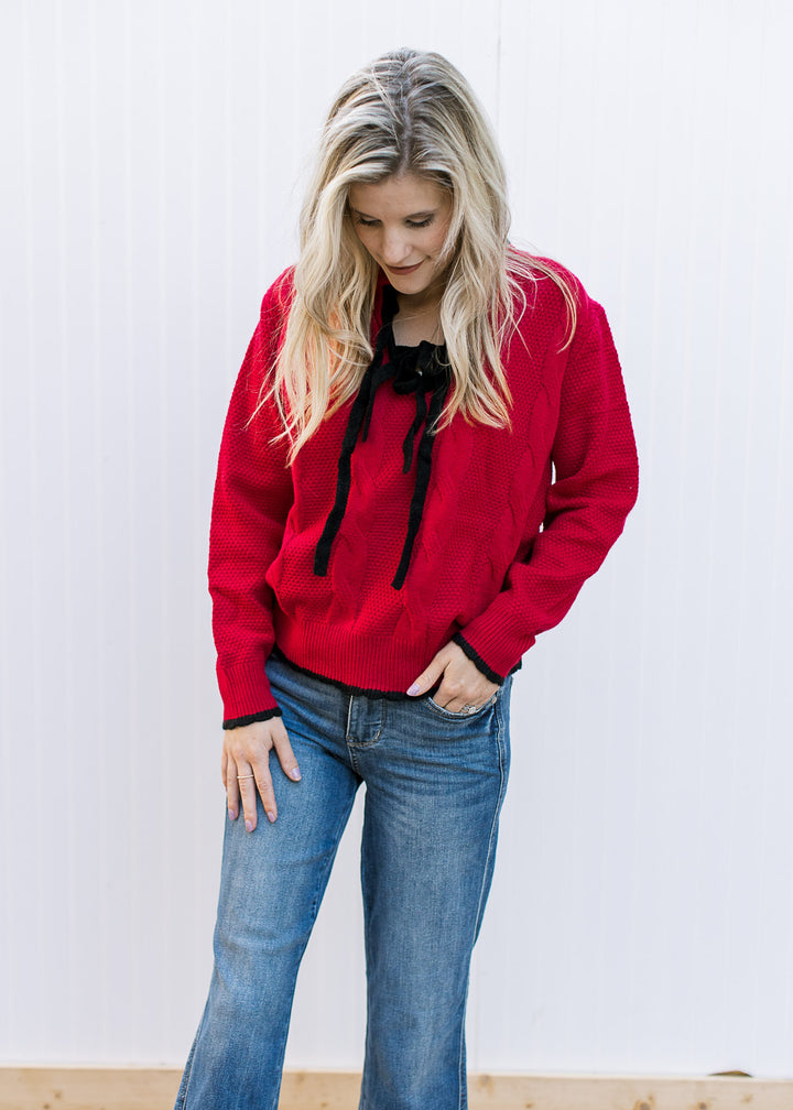 Model wearing jeans and a red knit sweater with black tie bow at v-neck and long sleeves.