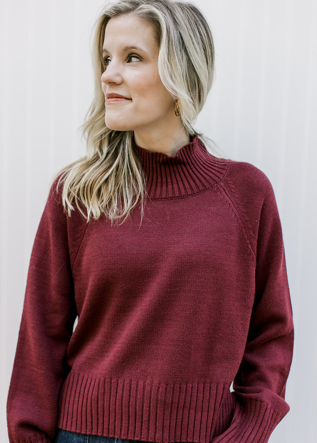 Model wearing a deep burgundy knit with a mock neckline, long sleeves and a slightly cropped fit.