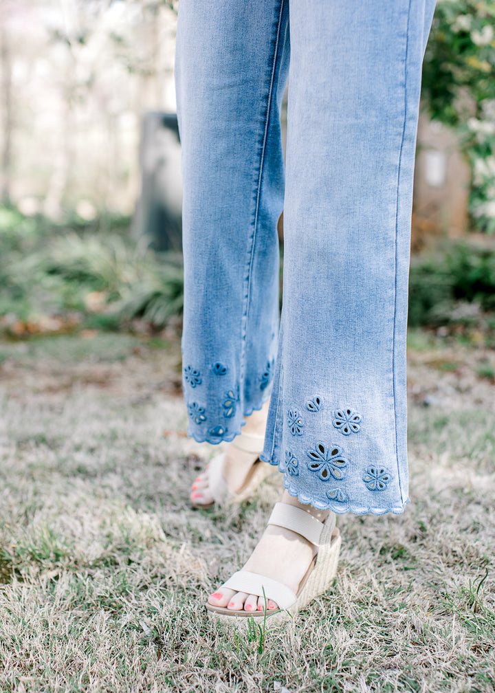 Model wearing medium wash jeans with a cropped wide leg fit and an open cut floral motif at hem.