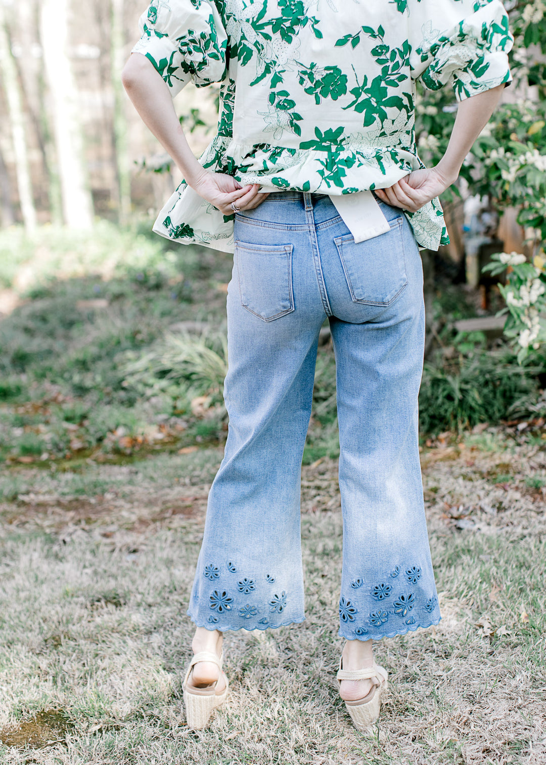 Back view of Model wearing medium wash jeans with a cropped wide leg fit and a floral motif at hem.