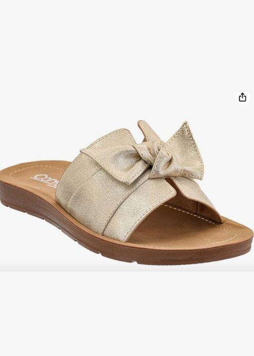 Front of a gold slip on sandal with a single wide strap with bow detail and a cushioned footbed.
