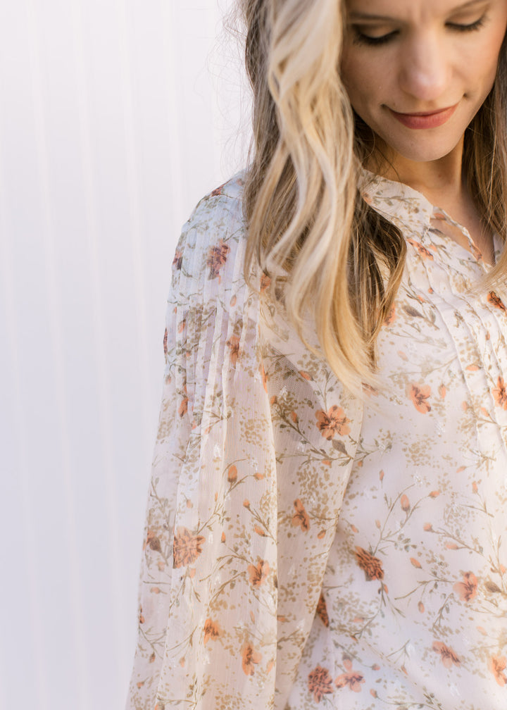 Close up of micro pleating at shoulder of sheer sleeves on a cream top with russet and green flowers.