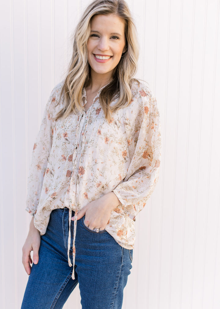 Model wearing a cream top with russet and green floral v-neck top with 3/4 sheer sleeves.