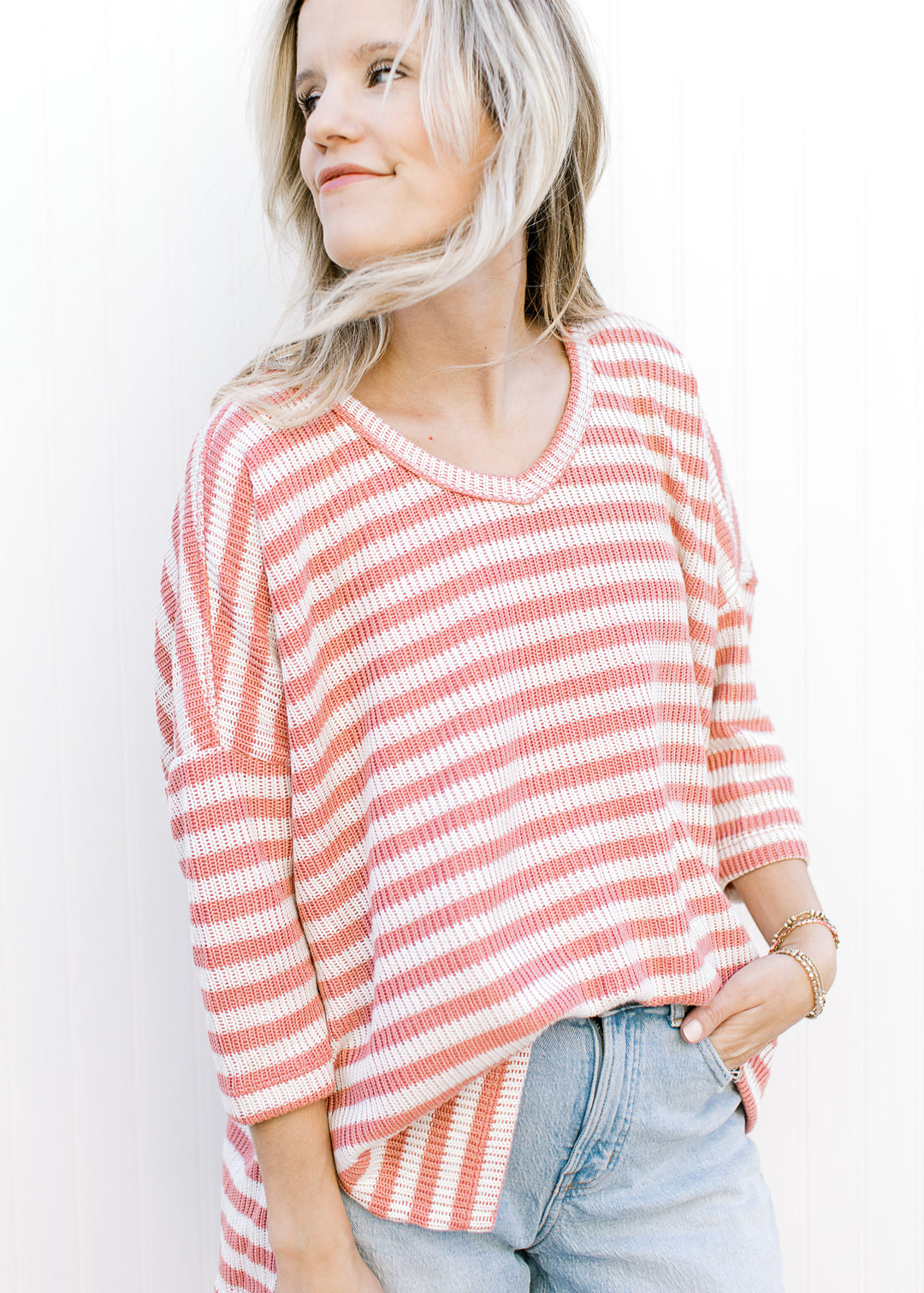 Model wearing a knit cream and rose striped top with v-neck, side slit and elbow length sleeves.