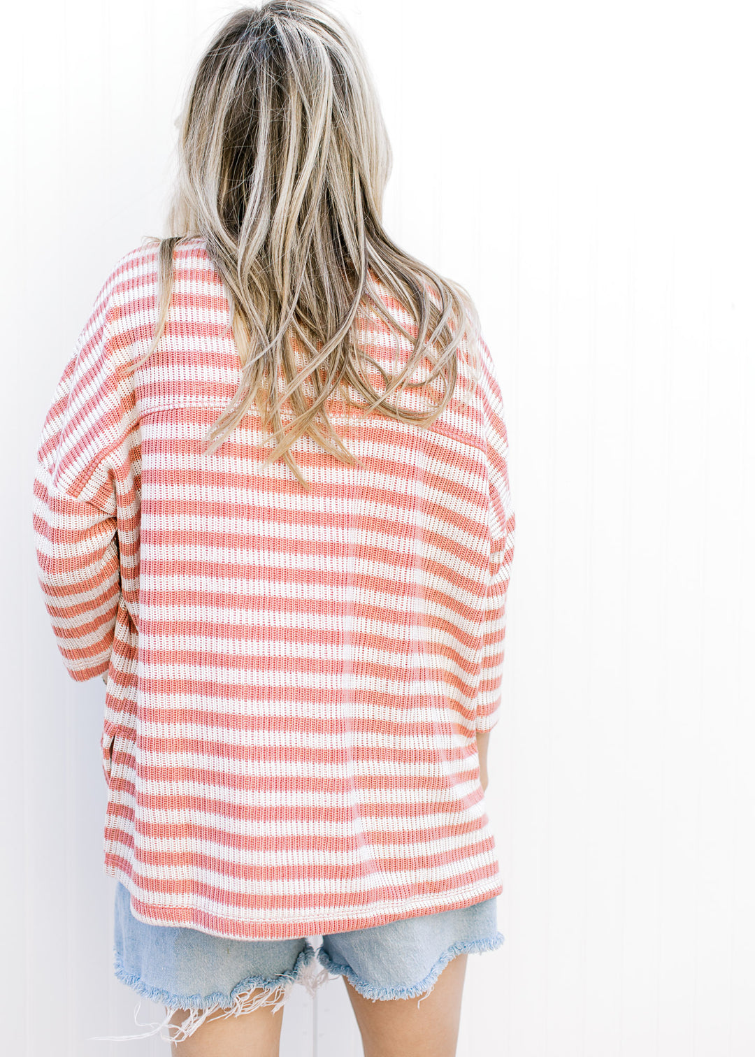 Back view of Model wearing a knit cream and rose striped top with side slit and 3/4 sleeves.