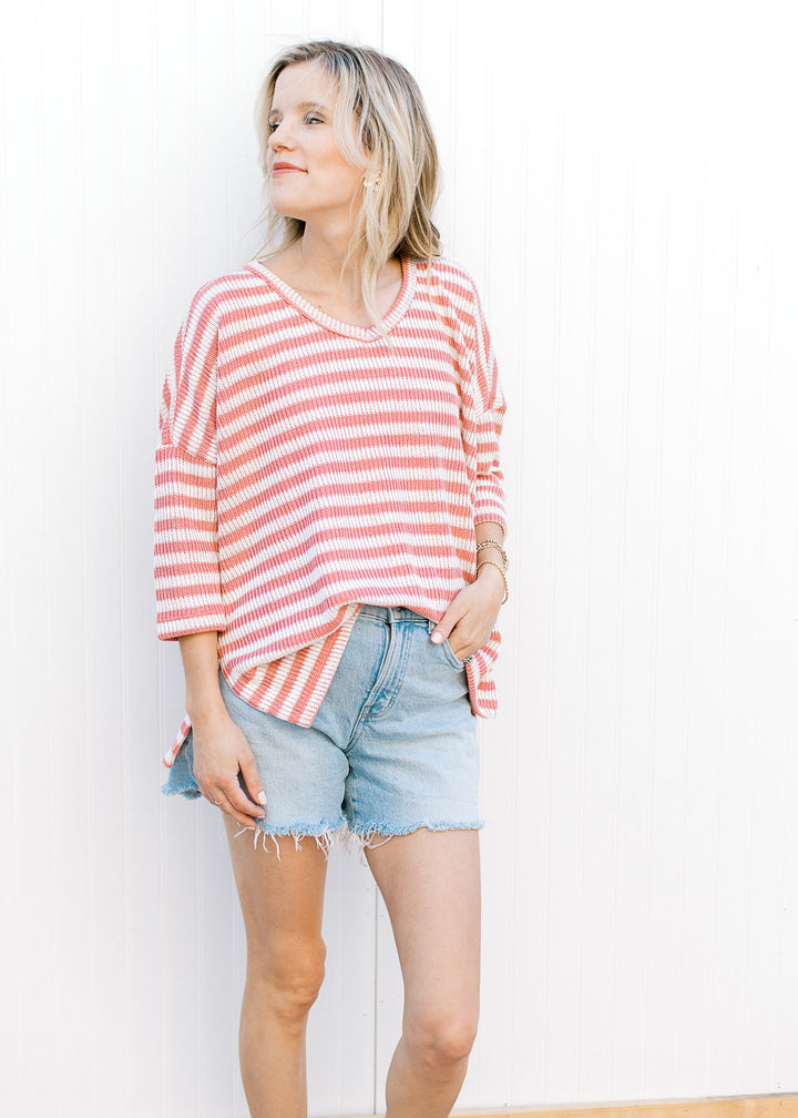 Model wearing shorts and a knit cream and rose striped top with side slit and elbow length sleeves.