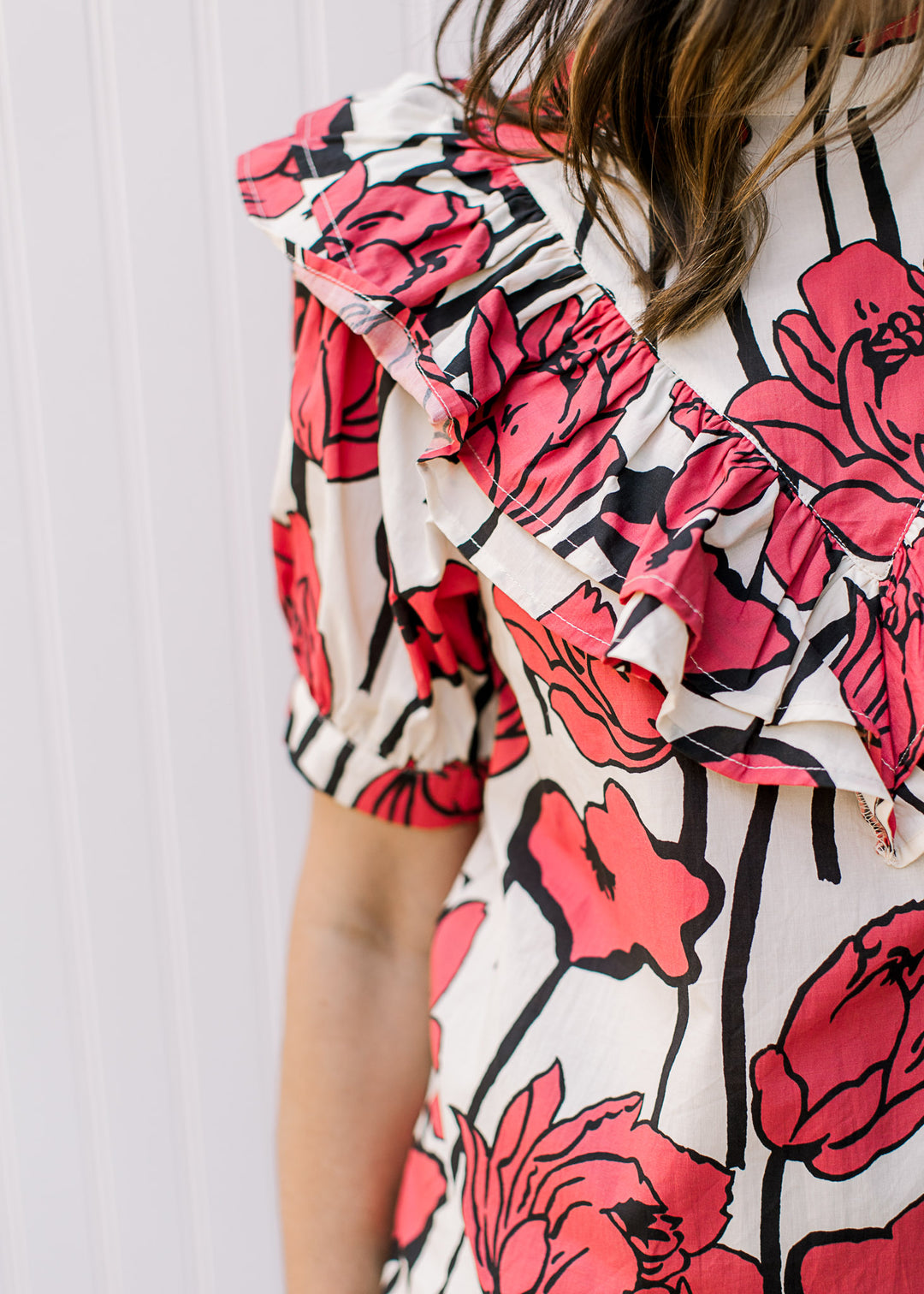 Close up of ruffle bib on a cream top with rose colored flowers, comprised of cotton.