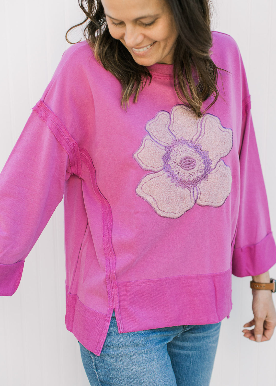 Model wearing a pink top with a stitched rose, side splits, 3/4 sleeves and exposed hem.