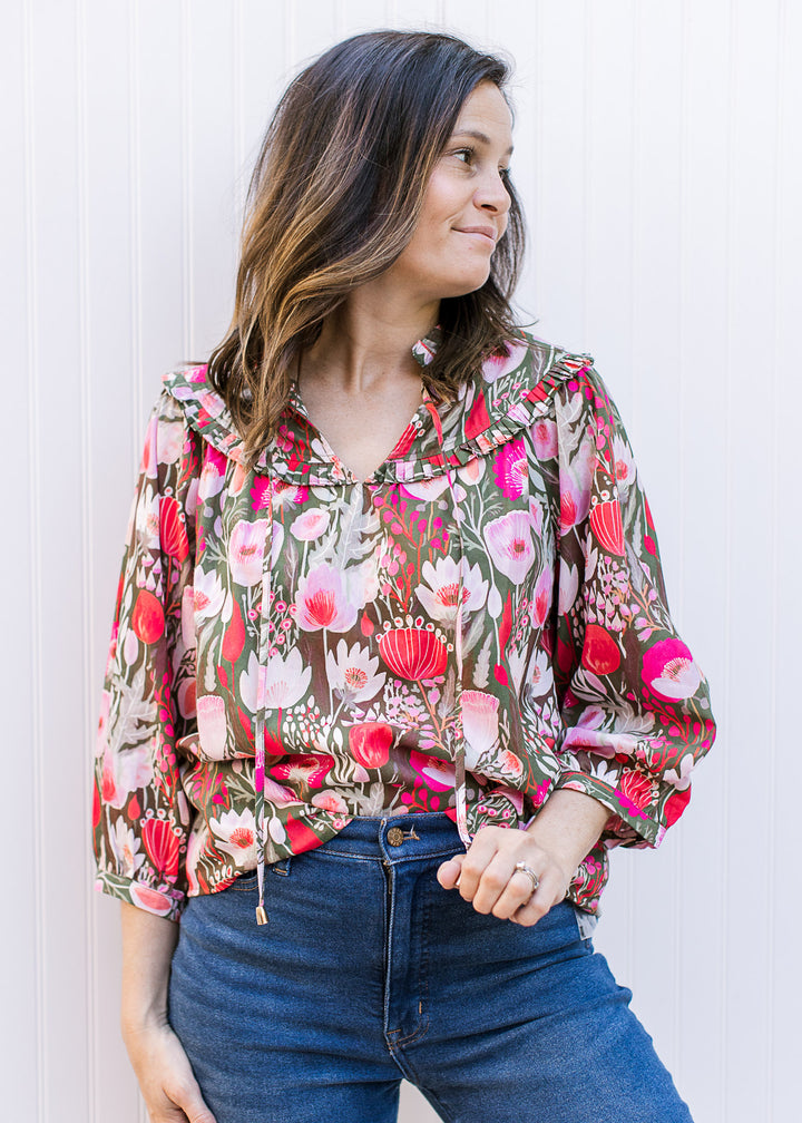 Model wearing a brown top with pink flowers, 3/4 sleeves and ruffle at neck and yolk.