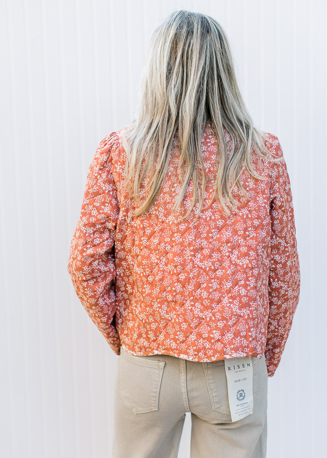 Back view of Model wearing a rust jacket with cream flowers, quilted material and two tie closure.