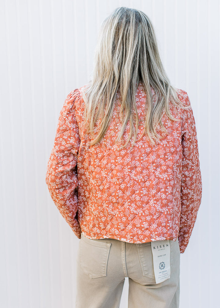 Back view of Model wearing a rust jacket with cream flowers, quilted material and two tie closure.