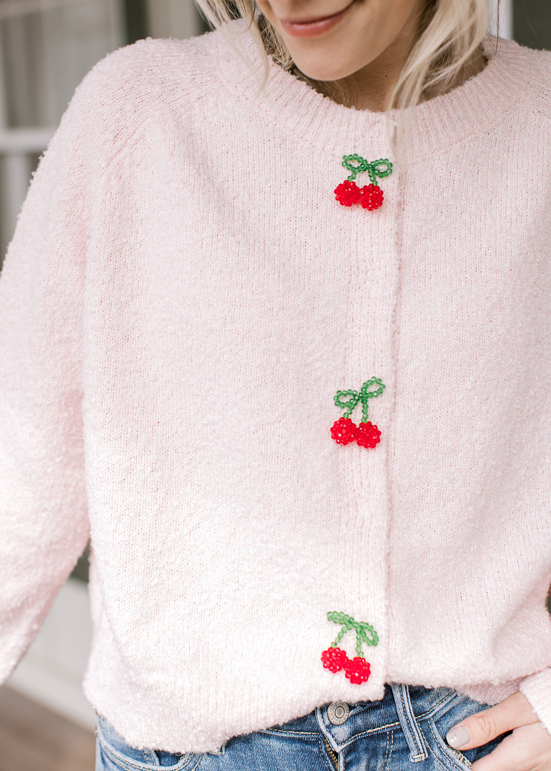Model wearing a pink cardigan with three cherry beaded clasp closure and long sleeves.