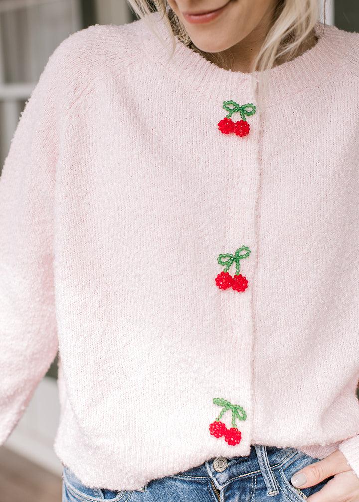 Model wearing a pink cardigan with three cherry beaded clasp closure and long sleeves.