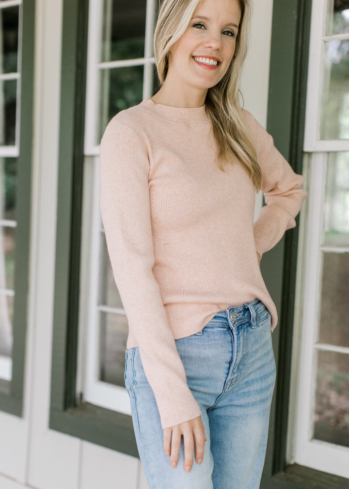 Model wearing a lightweight blush sweater with ribbed material, mock neck and long sleeves.