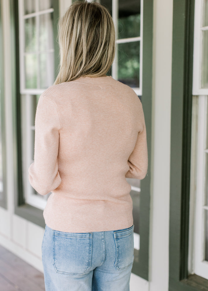 Back view of Model wearing a lightweight blush sweater with ribbed material and long sleeves.
