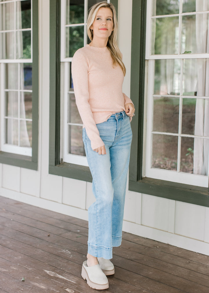Model wearing jeans, mules and a blush sweater with ribbed material, mock neck and long sleeves.
