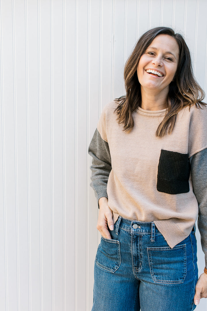 Model wearing a camel sweater with gray sleeves and a black patch pocket.
